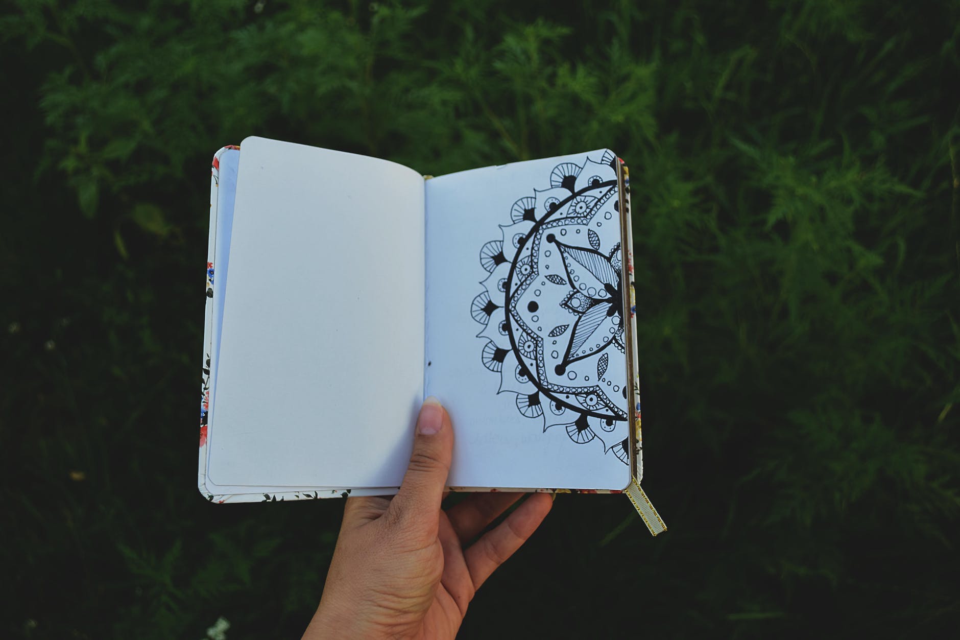 person holding open book with floral drawing